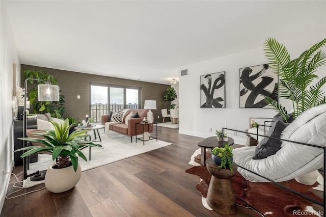 living room with visible vents, brick wall, baseboards, and wood finished floors