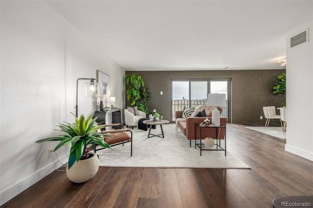 living area with hardwood / wood-style flooring, baseboards, visible vents, and brick wall