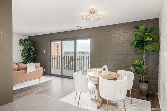 dining area featuring a notable chandelier, brick wall, and wood finished floors