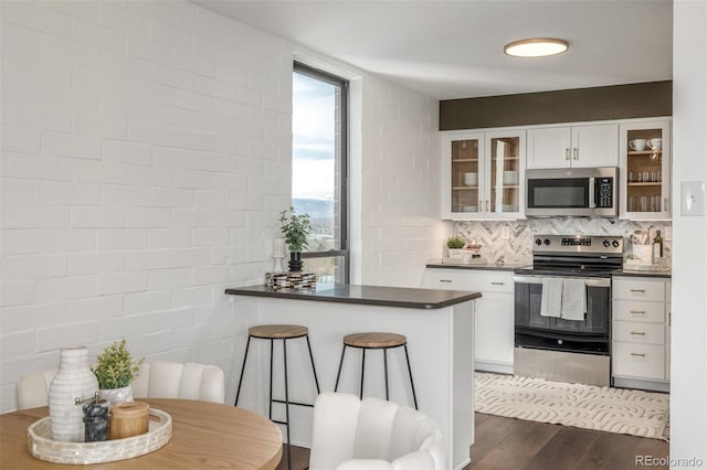 kitchen featuring dark countertops, glass insert cabinets, dark wood-type flooring, appliances with stainless steel finishes, and white cabinets