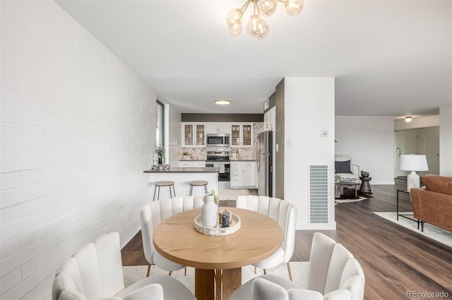 dining space featuring dark wood finished floors, an inviting chandelier, visible vents, and brick wall