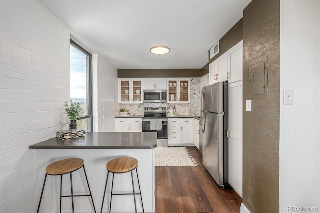 kitchen featuring dark wood-type flooring, dark countertops, stainless steel appliances, a peninsula, and glass insert cabinets