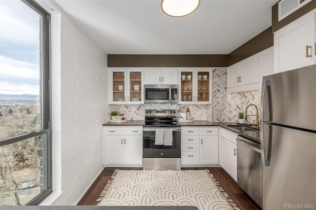 kitchen with a sink, dark countertops, dark wood finished floors, appliances with stainless steel finishes, and white cabinets