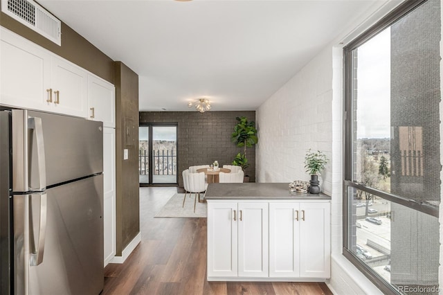 kitchen with visible vents, brick wall, freestanding refrigerator, white cabinets, and dark wood-style flooring