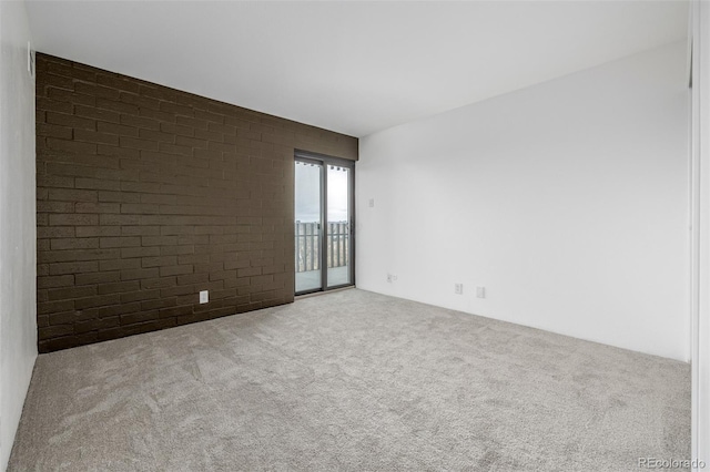 carpeted empty room featuring brick wall