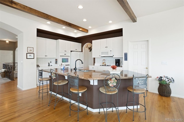 kitchen featuring sink, a large island with sink, white appliances, and beam ceiling