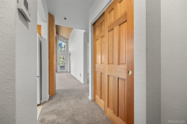 hall featuring a textured wall, baseboards, and carpet floors