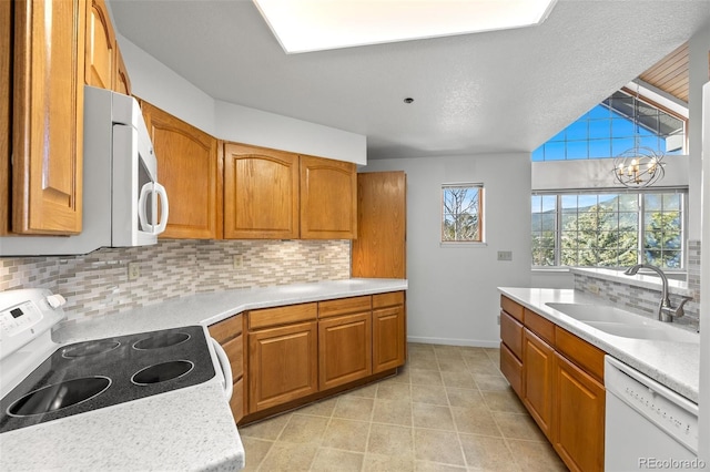 kitchen with white appliances, brown cabinetry, a sink, light countertops, and a notable chandelier