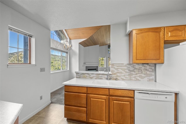 kitchen with brown cabinets, a sink, backsplash, white dishwasher, and light countertops