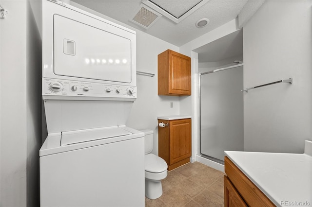 bathroom featuring visible vents, toilet, a stall shower, and stacked washer / dryer