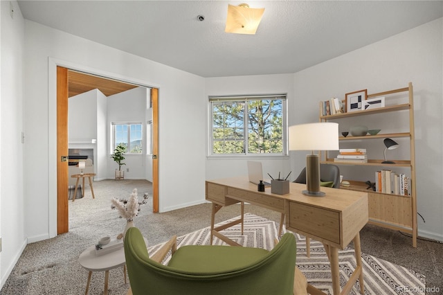 carpeted office space featuring baseboards and a tile fireplace