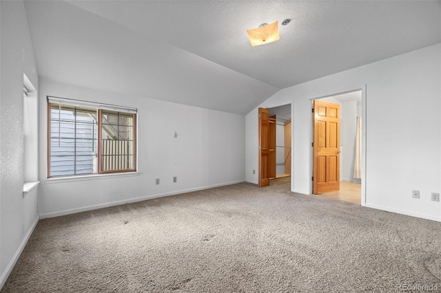 unfurnished bedroom featuring baseboards, lofted ceiling, a spacious closet, a textured ceiling, and light carpet