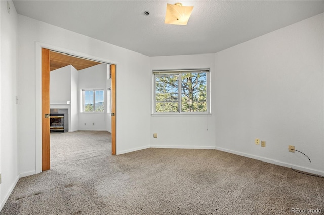 carpeted spare room featuring a fireplace with flush hearth, baseboards, and a textured ceiling