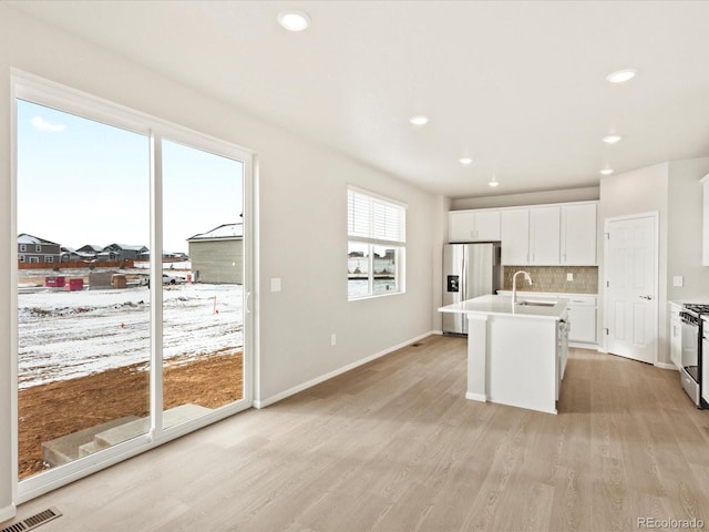 kitchen featuring stainless steel appliances, an island with sink, sink, backsplash, and light wood-type flooring