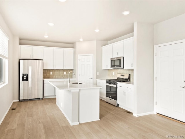 kitchen with white cabinets, light hardwood / wood-style flooring, stainless steel appliances, sink, and a center island with sink