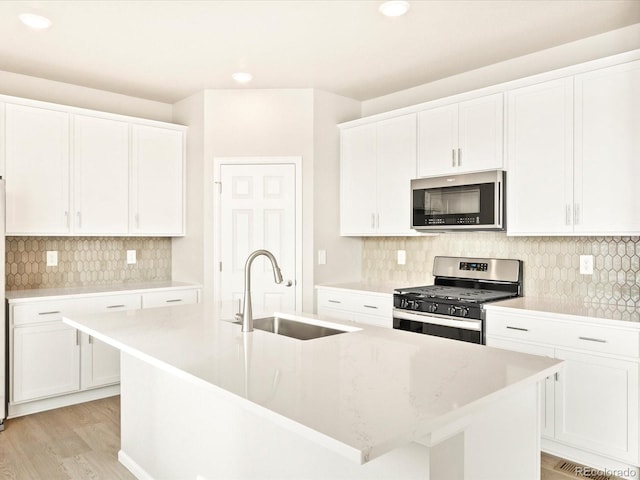 kitchen with a center island with sink, appliances with stainless steel finishes, light wood-type flooring, white cabinets, and sink