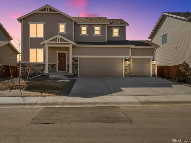 traditional home featuring stone siding, fence, driveway, and an attached garage