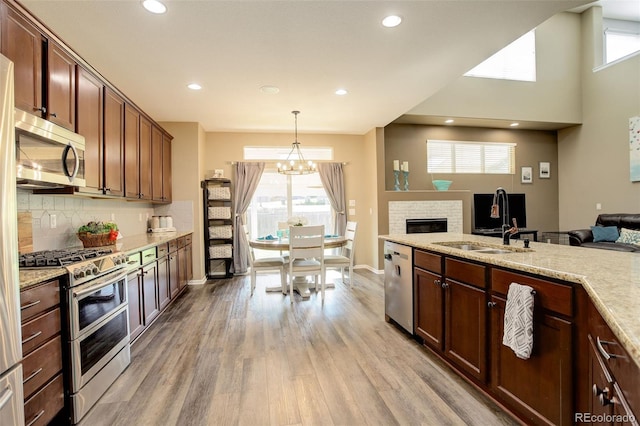 15122 Fillmore Way, Thornton, CO 80602 - kitchen featuring appliances with stainless steel finishes, open floor plan, a fireplace, light wood finished floors, and decorative backsplash