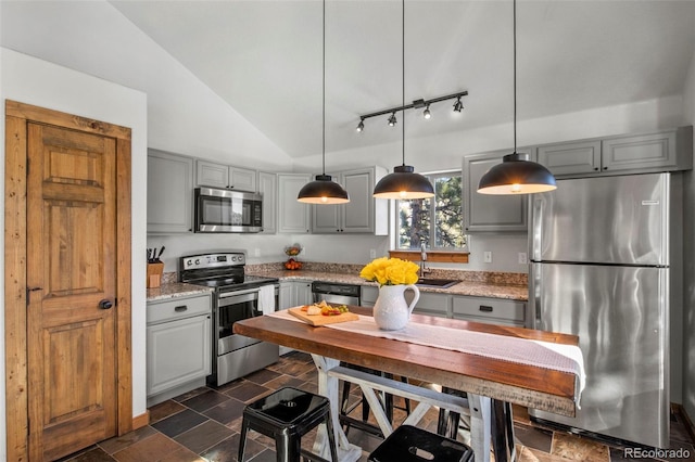 kitchen with lofted ceiling, gray cabinetry, a sink, appliances with stainless steel finishes, and stone finish floor