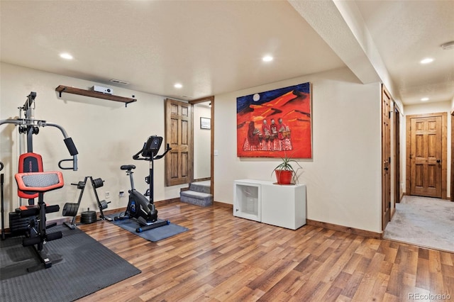 exercise room featuring baseboards, a textured ceiling, light wood-style flooring, and recessed lighting