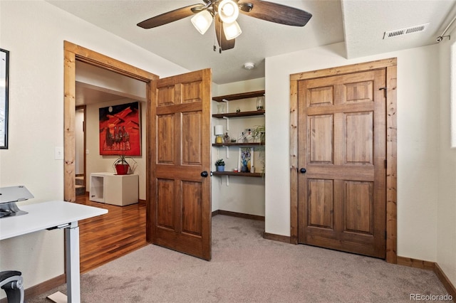 office space with light carpet, a ceiling fan, visible vents, and baseboards