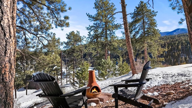 yard layered in snow featuring an outdoor fire pit, a wooded view, and a mountain view