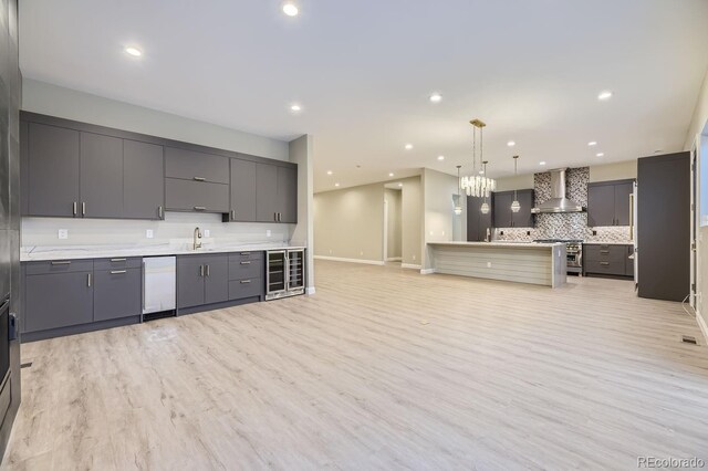 kitchen with light wood-type flooring, gray cabinets, wall chimney range hood, pendant lighting, and stainless steel range