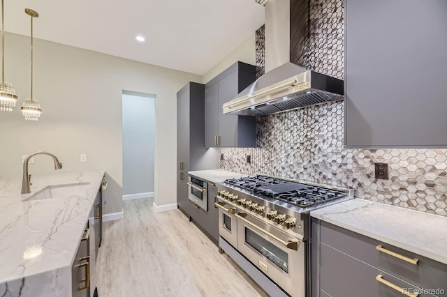 kitchen with light stone counters, wall chimney exhaust hood, sink, appliances with stainless steel finishes, and decorative light fixtures