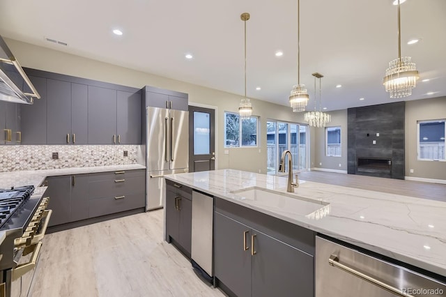 kitchen with sink, light stone counters, decorative light fixtures, light hardwood / wood-style flooring, and premium appliances