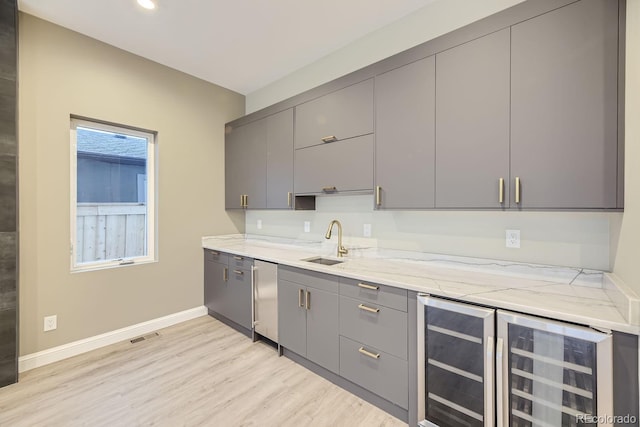 kitchen featuring gray cabinets, light wood-type flooring, sink, and light stone countertops