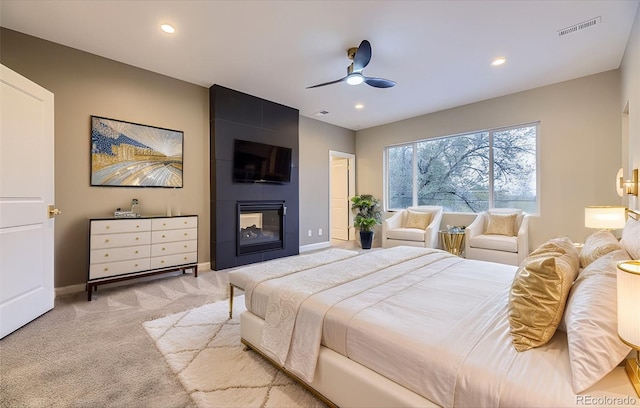 bedroom featuring a large fireplace, light colored carpet, and ceiling fan