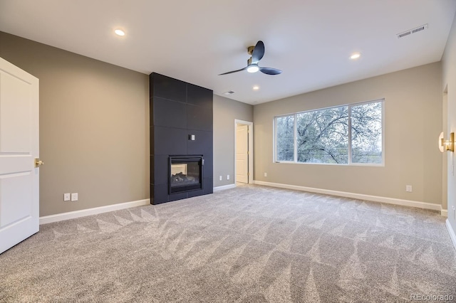 unfurnished living room with ceiling fan, a tiled fireplace, and carpet