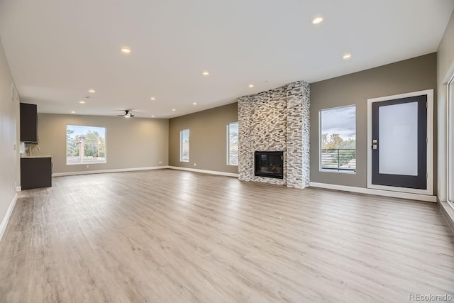 unfurnished living room with ceiling fan, a stone fireplace, and light hardwood / wood-style flooring