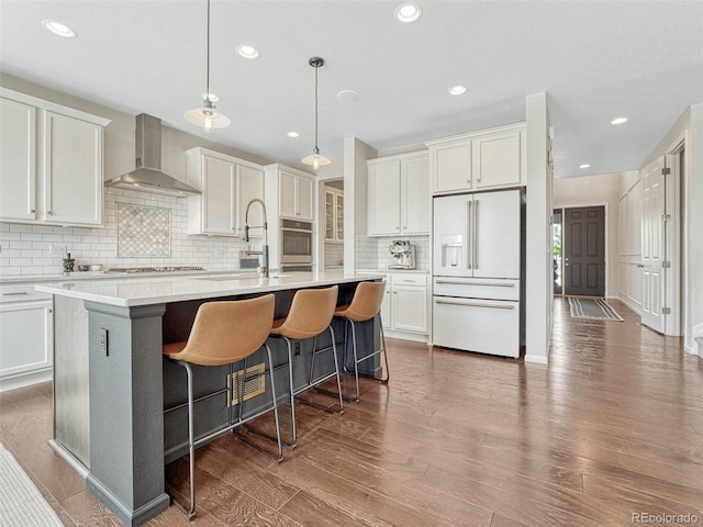 kitchen featuring hardwood / wood-style flooring, stainless steel appliances, sink, wall chimney exhaust hood, and a center island with sink