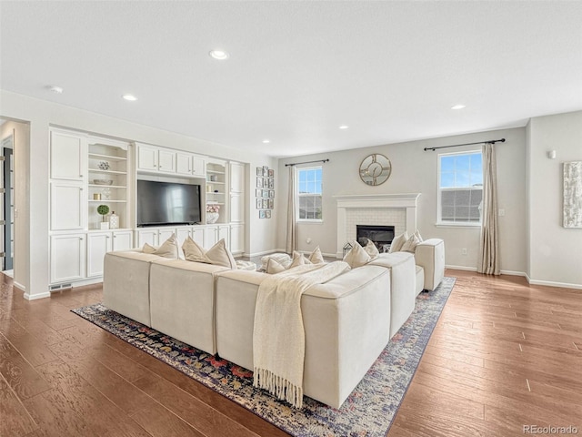 living room with a wealth of natural light, hardwood / wood-style floors, and a brick fireplace