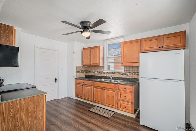 kitchen featuring dark countertops, a sink, freestanding refrigerator, a ceiling fan, and backsplash