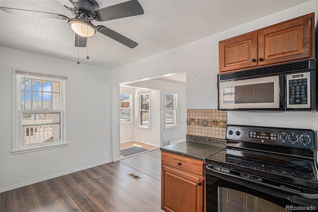 kitchen with dark countertops, black electric range, brown cabinetry, stainless steel microwave, and dark wood-style floors