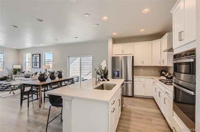 kitchen featuring appliances with stainless steel finishes, sink, white cabinetry, light hardwood / wood-style flooring, and a center island with sink