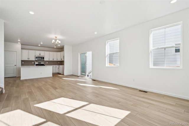 unfurnished living room with a chandelier and light hardwood / wood-style floors