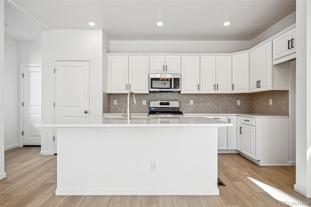 kitchen with white cabinetry, stainless steel appliances, a kitchen island with sink, and light hardwood / wood-style flooring