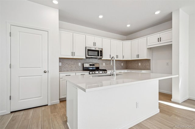 kitchen with white cabinetry, appliances with stainless steel finishes, light hardwood / wood-style floors, and an island with sink