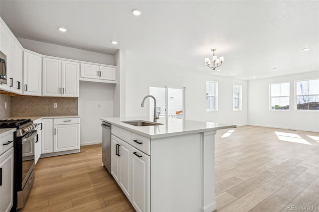 kitchen featuring appliances with stainless steel finishes, tasteful backsplash, white cabinetry, sink, and a center island with sink