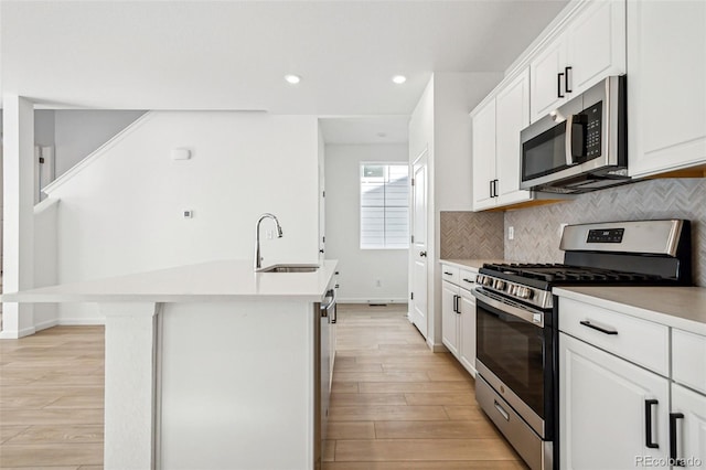 kitchen with sink, stainless steel appliances, an island with sink, white cabinets, and decorative backsplash