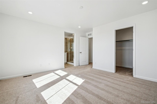 unfurnished bedroom with ensuite bathroom, a spacious closet, light colored carpet, and a closet