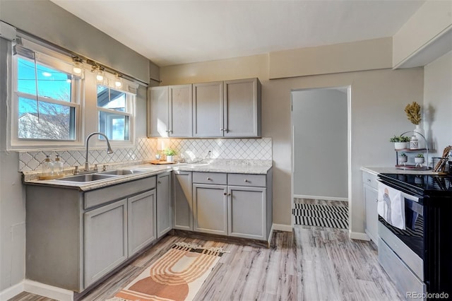 kitchen with light wood finished floors, decorative backsplash, gray cabinets, stainless steel range with electric stovetop, and a sink