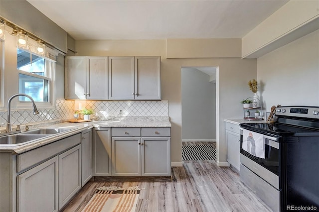 kitchen featuring gray cabinetry, a sink, stainless steel electric range, decorative backsplash, and light wood finished floors