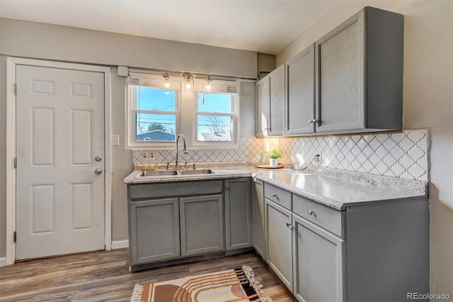 kitchen featuring tasteful backsplash, light wood-style flooring, light countertops, gray cabinetry, and a sink