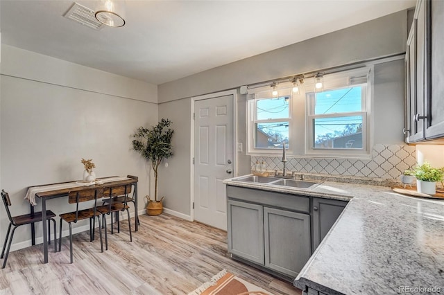 kitchen featuring tasteful backsplash, visible vents, gray cabinetry, light wood-type flooring, and a sink