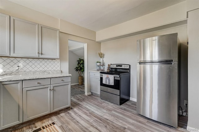 kitchen featuring light stone counters, stainless steel appliances, gray cabinets, light wood-style flooring, and backsplash