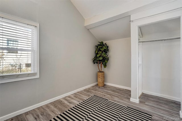 unfurnished bedroom featuring lofted ceiling, a closet, baseboards, and wood finished floors